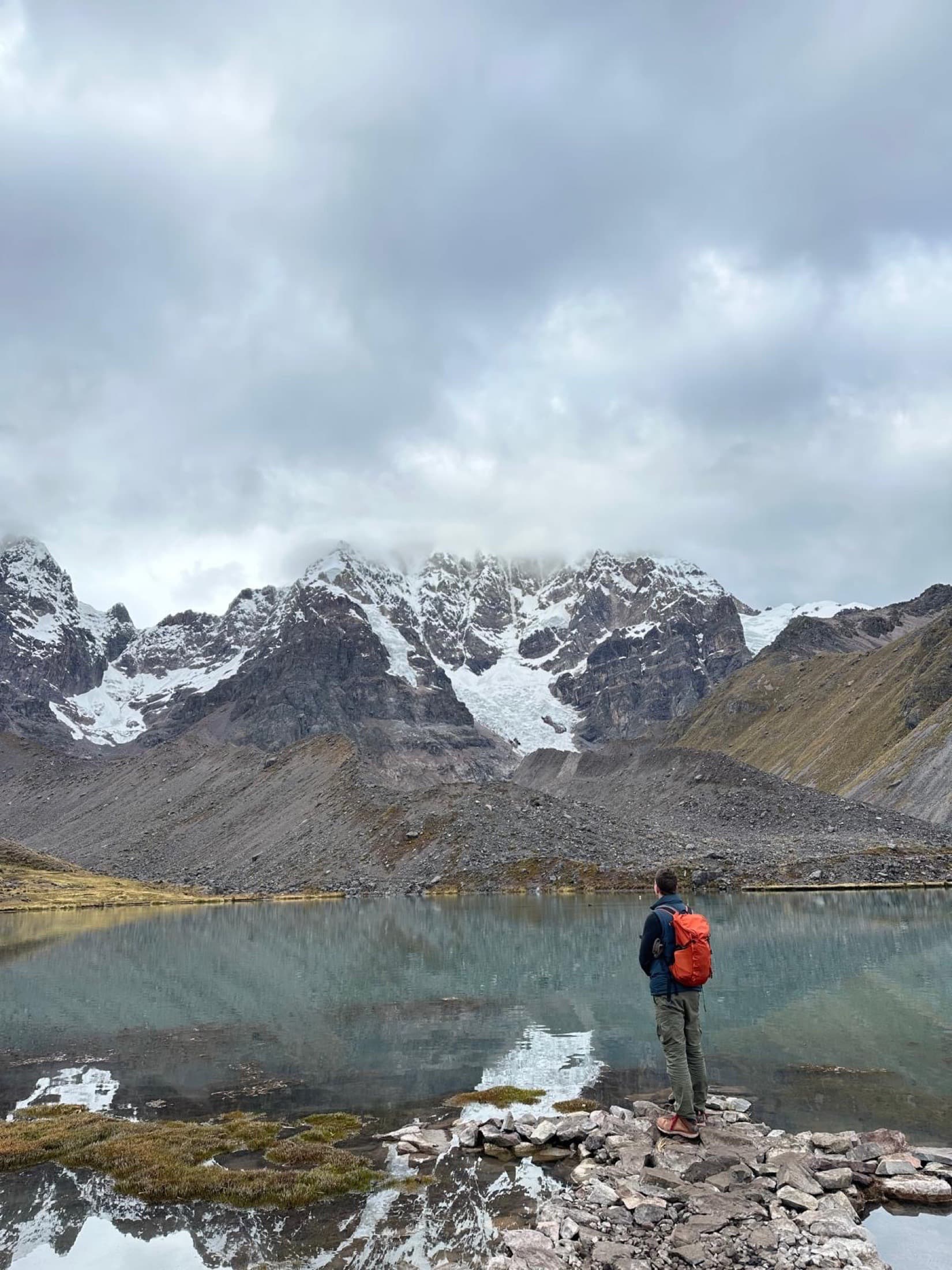 Christopher Heinrich facing a mountain lake beneath snow-covered peaks